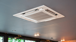 Ceiling-mounted cassette air conditioner unit on a gray ceiling in a modern room.