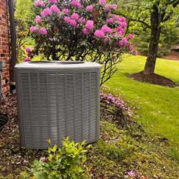 home air conditioner unit next to a beautiful flowering bush