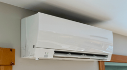 White wall-mounted air conditioner unit with its front vent open, installed on a light-colored wall near a window.
