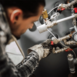 Maintenance technician adjusting valves on a metal piping system, wearing gloves in an industrial setting