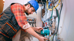 Technician wearing a blue hard hat and plaid shirt adjusts valves and cables in a utility panel.