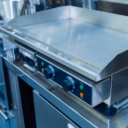 Professional flat-top griddle in a stainless steel kitchen, with two control knobs on the front panel.