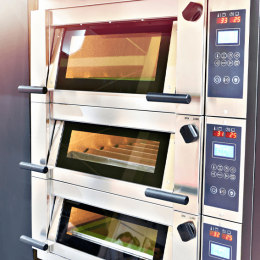 Triple-stack commercial convection oven with glass doors and horizontal handles in a bakery kitchen, metal control panel on the right.