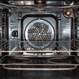 Interior of a metal oven cavity with two wire racks, a circular convection fan at the back, and bottom heating elements visible.