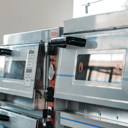 Two stainless steel commercial ovens with glass doors and black handles in a bakery or kitchen setting.