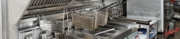 Commercial dishwashing station with wire baskets hanging above a stainless steel conveyor system in a busy kitchen.