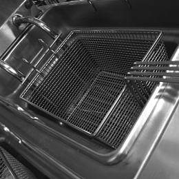 Inside a stainless steel deep fryer, a metal wire basket sits in the oil basin with long handles extending outward.