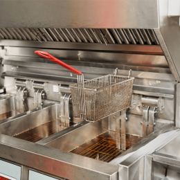 Commercial deep fryer with a metal basket about to be lowered into hot oil, red handle visible in a professional kitchen