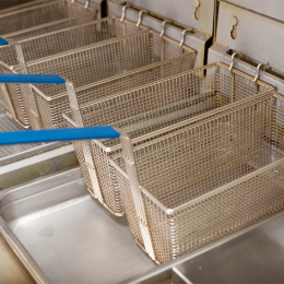 Stainless steel fryer baskets with blue handles resting on a metal rack in a commercial kitchen.