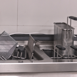 Commercial kitchen sink with stacked metal fryer baskets in a stainless steel trough against a tiled wall.