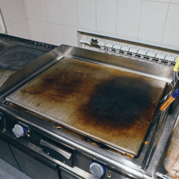 Commercial kitchen griddle with heavy grease and burnt spots on its stainless-steel surface.