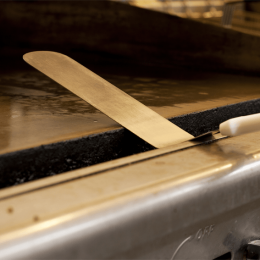 Metal spatula resting on a hot griddle in a kitchen, close-up. Used to flip food on the flat grill surface.