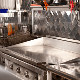 Commercial stainless steel kitchen with flat-top grill, utensil rack, and hanging tongs