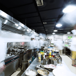 Busy commercial kitchen with blurred chefs working along a stainless steel prep line and pots and ingredients laid out on the counter
