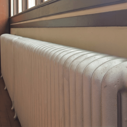 White cast-iron radiator with vertical fins running along a wooden floor beneath a window.