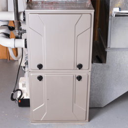 Two-section beige furnace/air handler in a basement, with black knobs on the doors and nearby piping