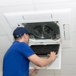 HVAC technician in a blue shirt and cap inspecting a ceiling-mounted vent with its cover removed